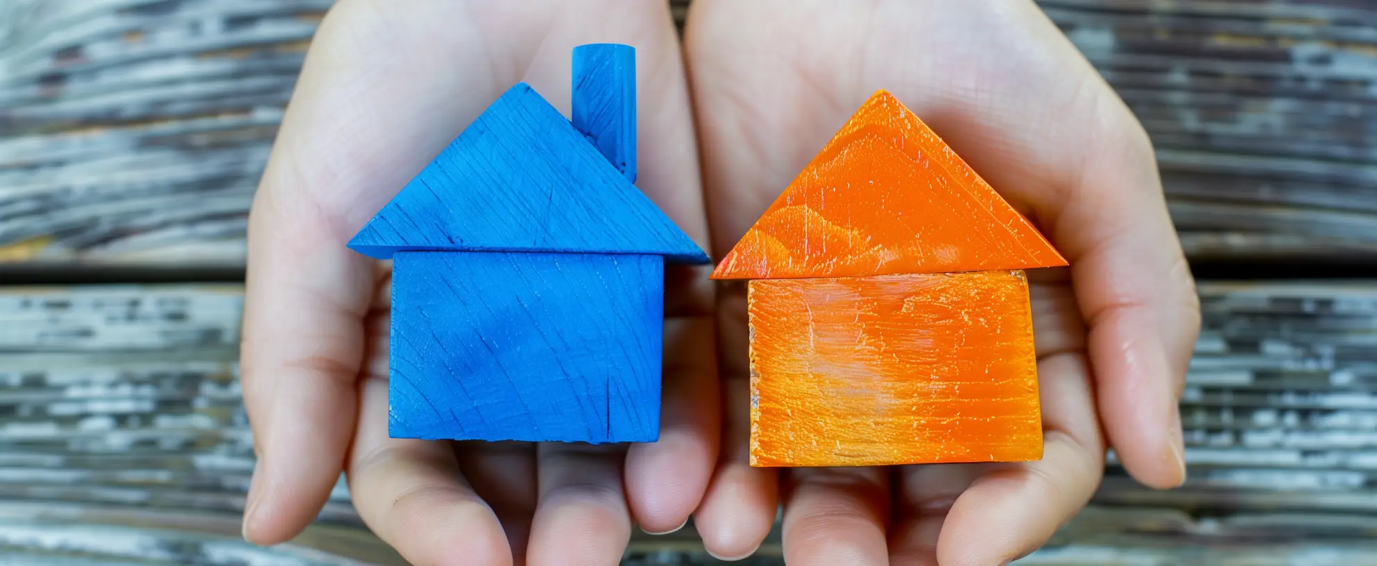Eine Hand hält ein orangenes und ein blaues Modell-Haus aus Holz